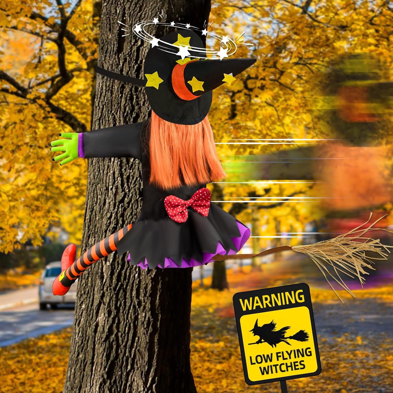 Crashing witch decoration hung against a tree trunk with a low flying witches warning sign