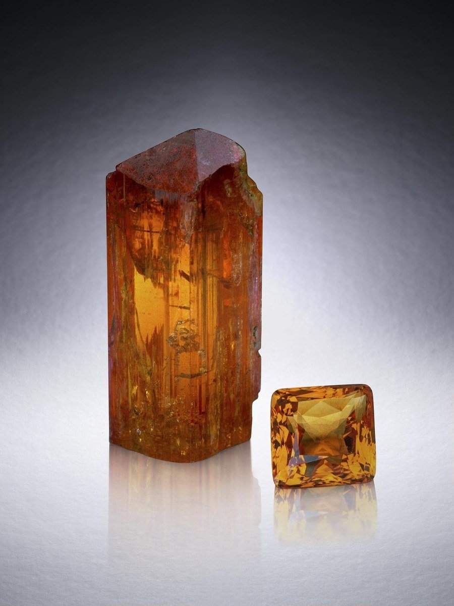 An orange imperial topaz crystal beside a 93.6-carat cut topaz