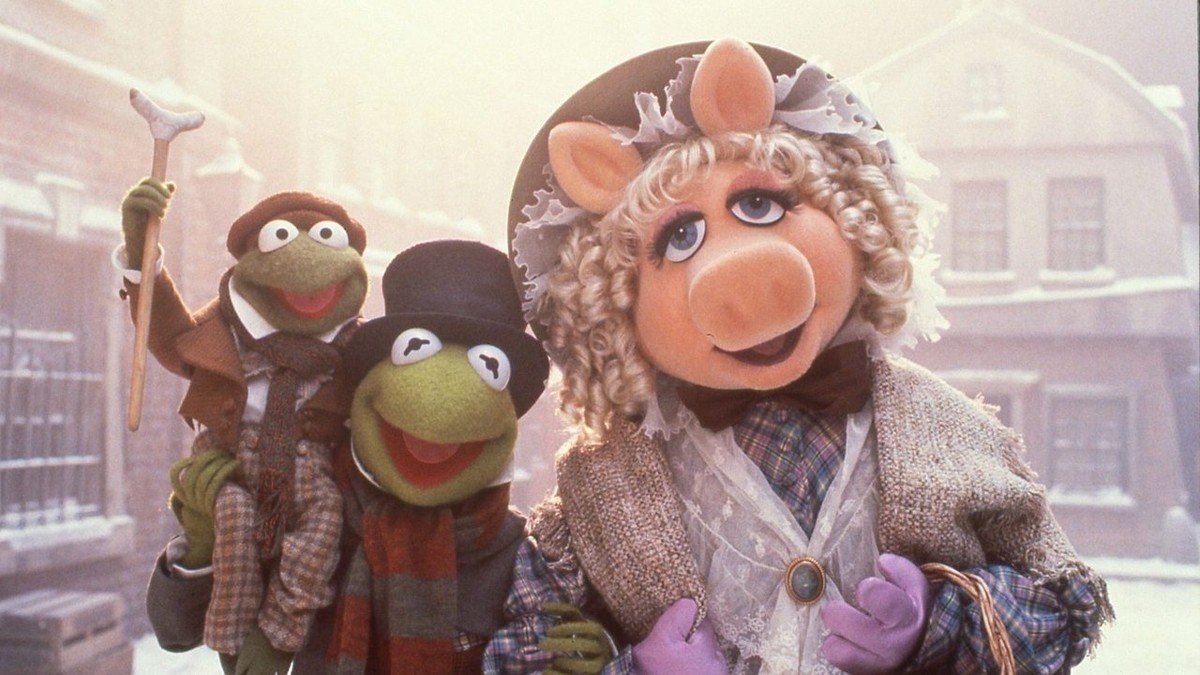 Still of Kermit as Bob Cratchit carrying Tiny Tim beside Miss Piggy on a snowy street
