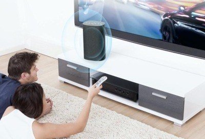 Two people on the floor in front of a Samsung TV with a Bluetooth speaker on the TV stand