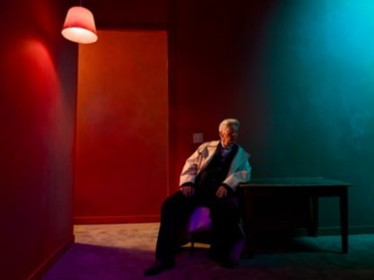 Person seated in a dimly lit red and teal room photographed on iPhone 18 Pro