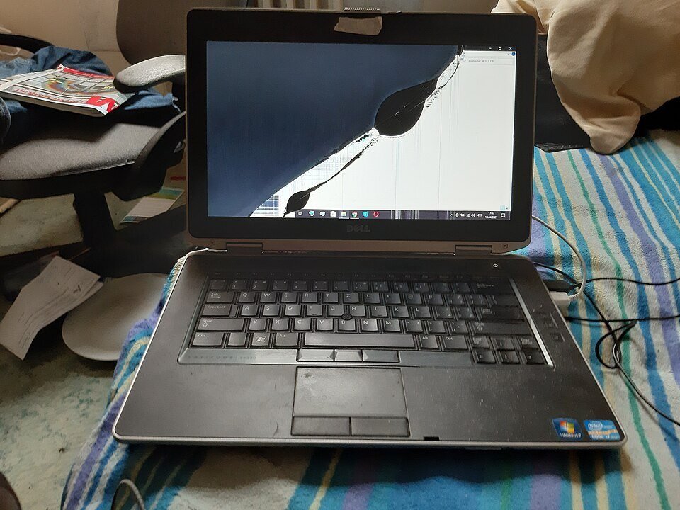 Dell laptop on a bed with a broken LCD showing a dark blot and lines spreading across the display