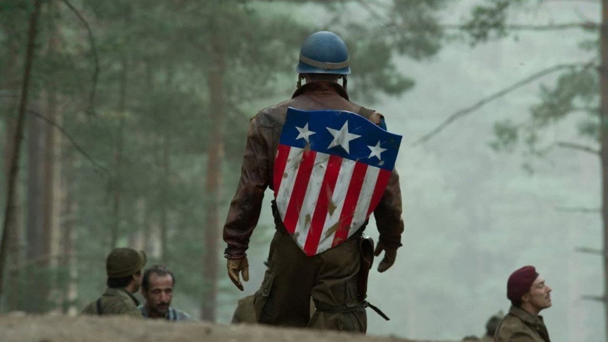 Steve Rogers walks through a forest carrying his early striped shield past soldiers