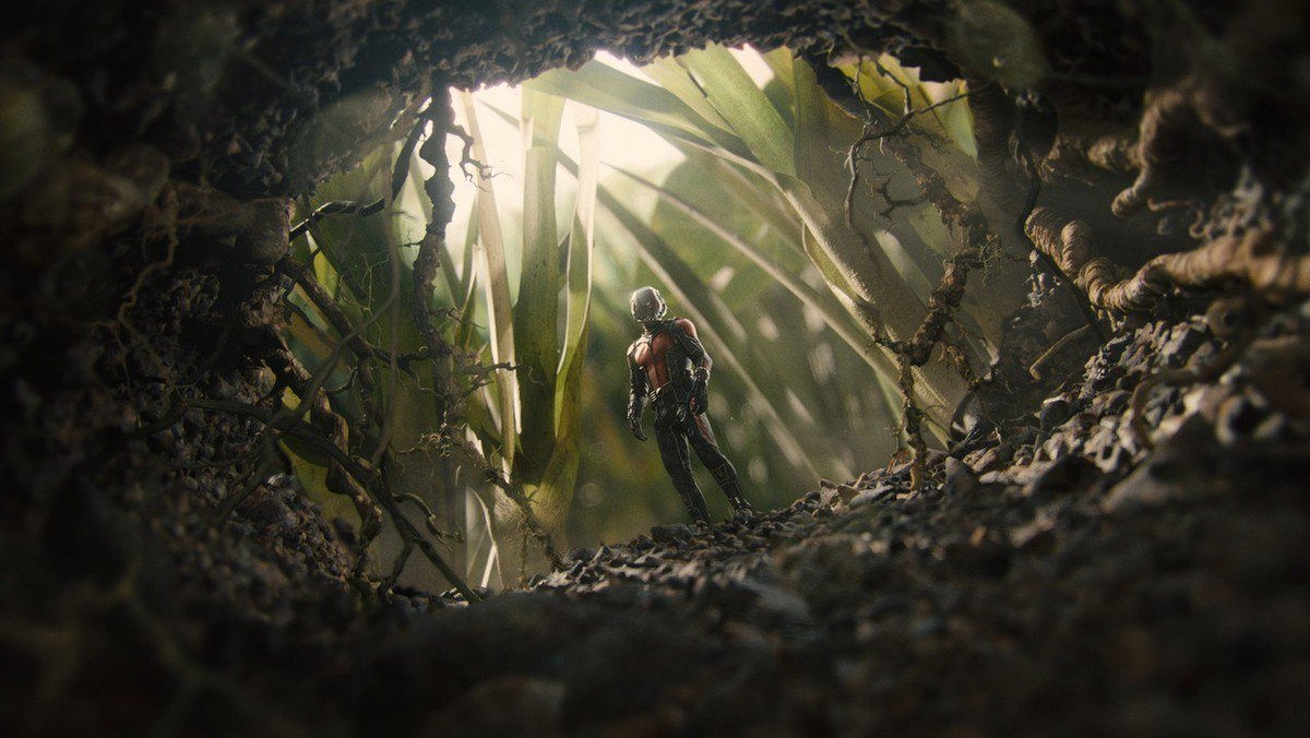 A tiny Ant-Man stands in a tunnel of soil and grass