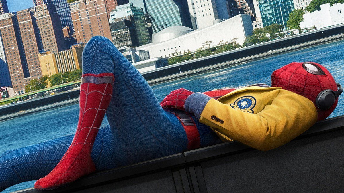 Spider-Man lies on a ledge by the river in a yellow jacket, with the Manhattan skyline behind him