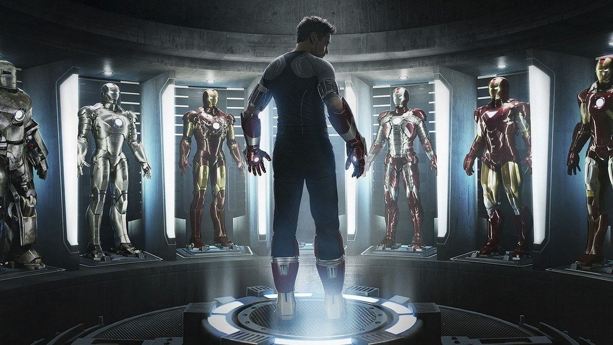 Tony Stark stands in a lit chamber lined with rows of Iron Man armors