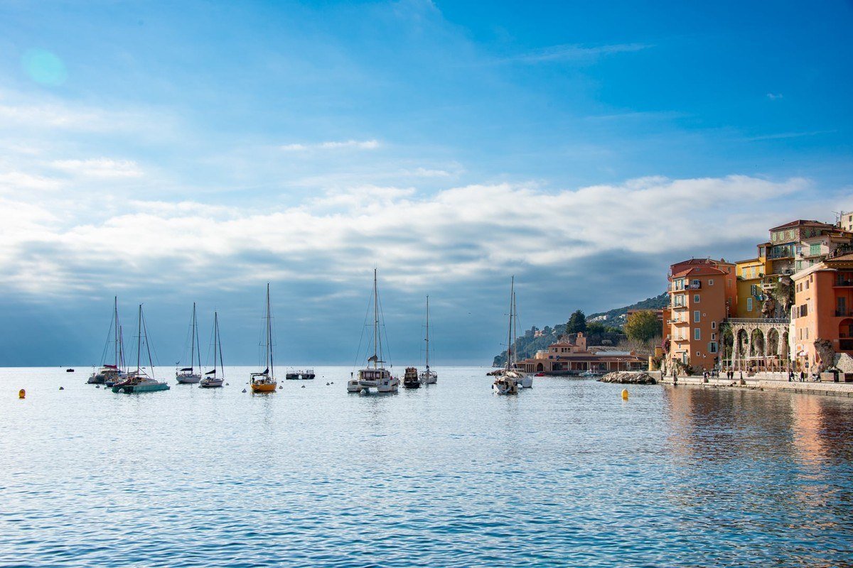 Sailing boats on the calm bay of Villefranche-sur-Mer with the pastel waterfront on the right