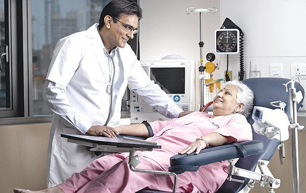 Doctor in a white coat checking the blood pressure of a seated patient in a treatment chair