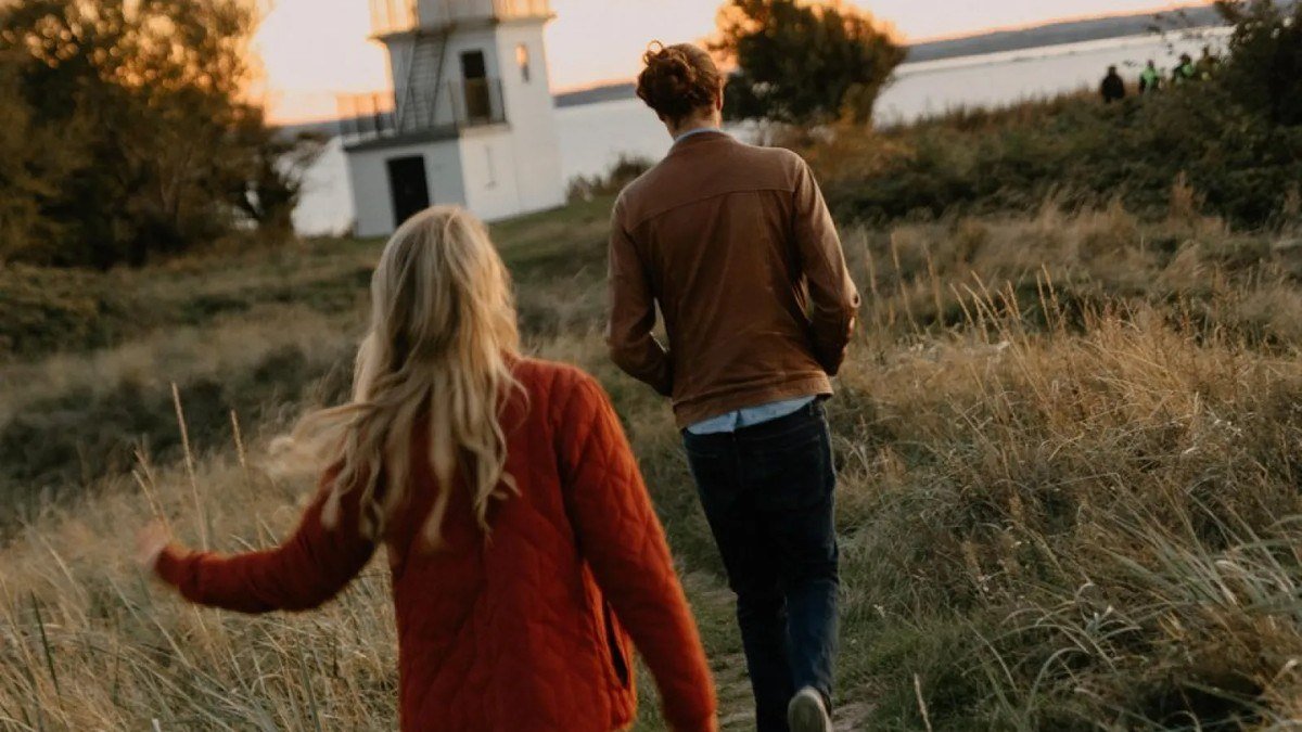 Couple walking toward a lighthouse on a grassy headland in Denmark